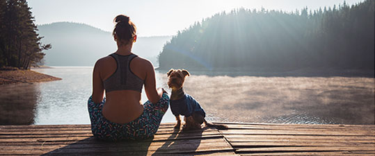 Woman and dog sitting by a lake meditating