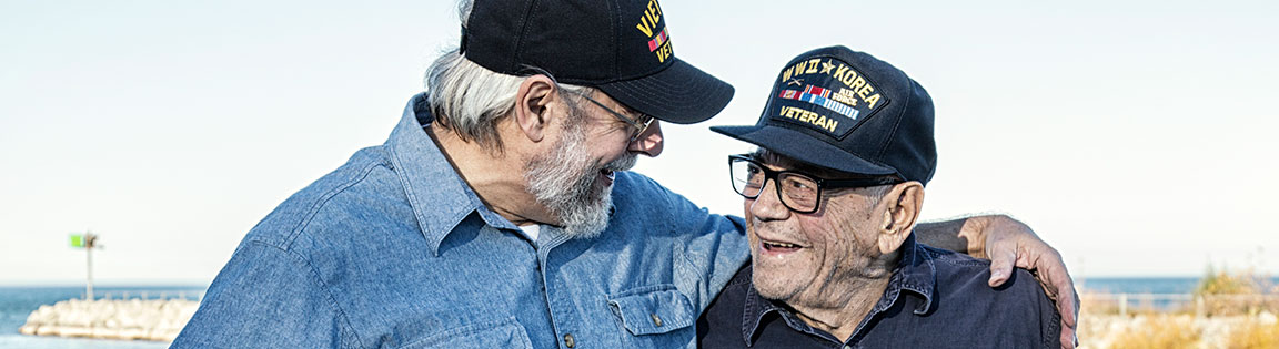 Two veterans laughing together as they stand near a body of water.