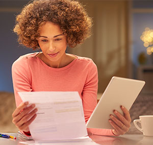 Young woman going through paperwork while holding a tablet in her home