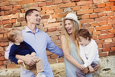 Family of four laughing together outside by a brick wall